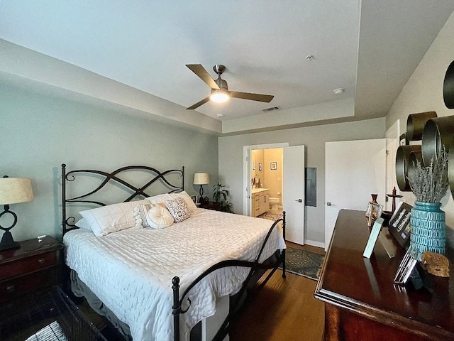 bedroom with a tray ceiling, ensuite bath, ceiling fan, and dark wood-type flooring