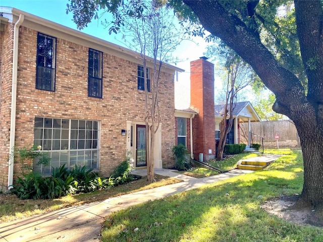 view of front of house with brick siding, a chimney, and fence