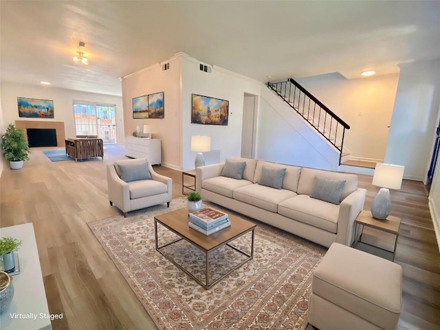 living area with stairs, wood finished floors, visible vents, and baseboards