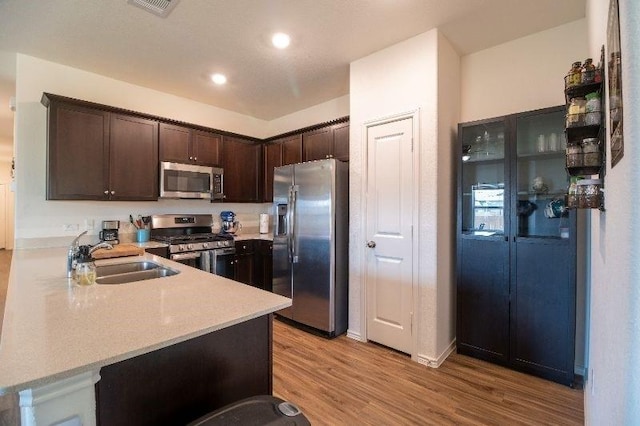 kitchen with kitchen peninsula, sink, light hardwood / wood-style floors, dark brown cabinetry, and stainless steel appliances