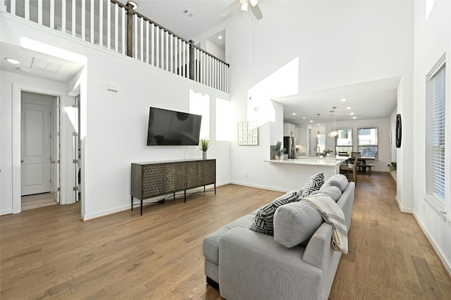 living room with a high ceiling, ceiling fan, and wood-type flooring