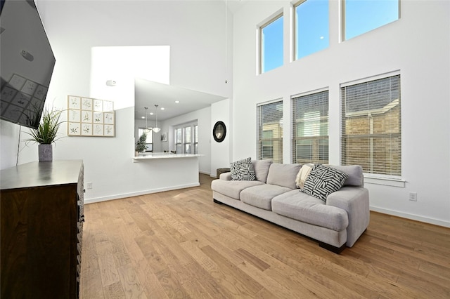 living area with light wood finished floors, a towering ceiling, and baseboards