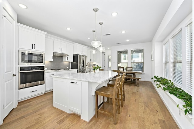 kitchen with white cabinets, decorative light fixtures, stainless steel appliances, and a center island with sink