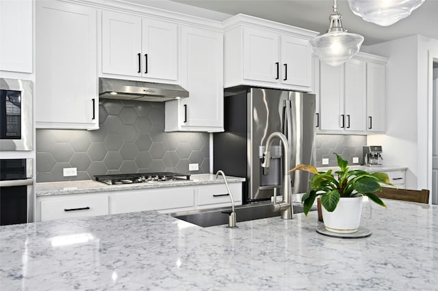 kitchen with appliances with stainless steel finishes, backsplash, white cabinetry, and under cabinet range hood