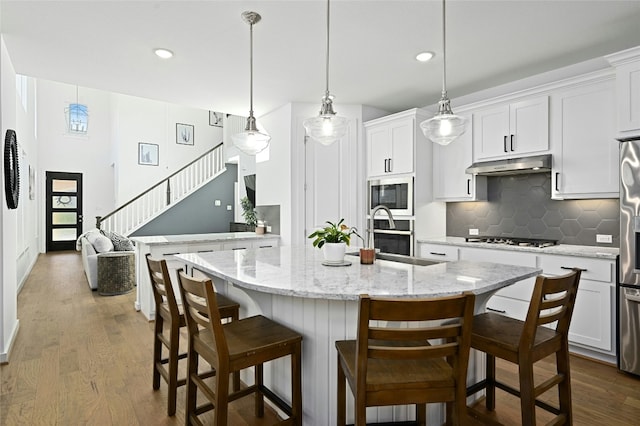 kitchen with dark wood-style floors, tasteful backsplash, appliances with stainless steel finishes, white cabinets, and under cabinet range hood