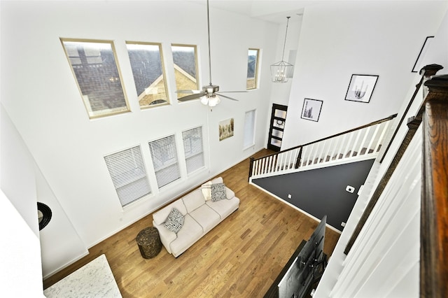 living area with a towering ceiling, stairs, wood finished floors, and ceiling fan with notable chandelier