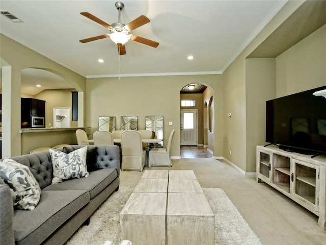 living room with ceiling fan, ornamental molding, and light carpet