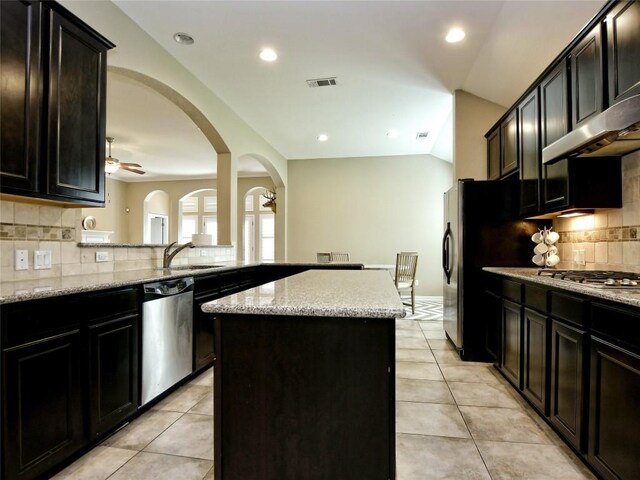 kitchen with ceiling fan, light tile patterned floors, a kitchen island, light stone counters, and stainless steel appliances