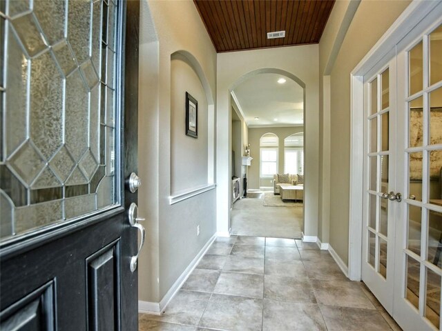 entrance foyer with light carpet, french doors, ornamental molding, and wood ceiling