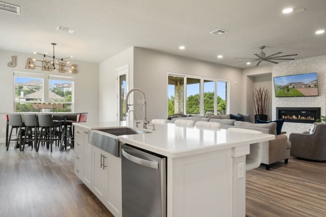 kitchen with a large fireplace, sink, a center island with sink, dishwasher, and white cabinetry