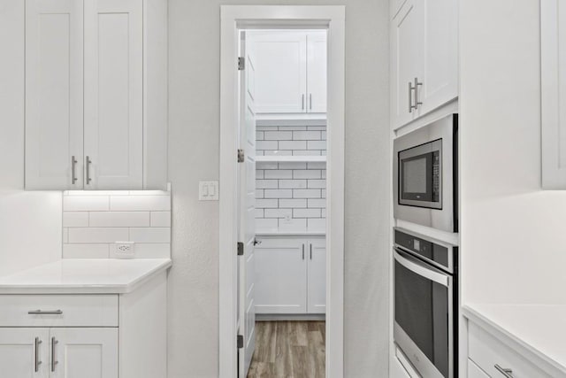 kitchen with built in microwave, tasteful backsplash, hardwood / wood-style floors, oven, and white cabinets