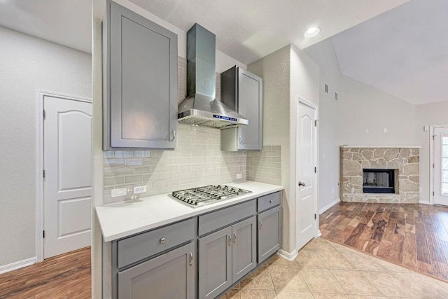 kitchen with gray cabinets, a fireplace, wall chimney range hood, and stainless steel gas stovetop