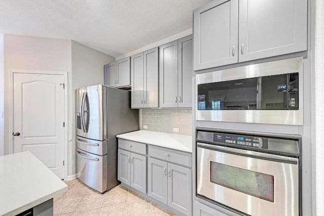 kitchen with gray cabinetry, stainless steel appliances, tasteful backsplash, a textured ceiling, and light tile patterned flooring