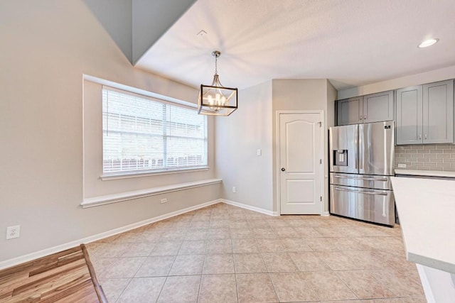 kitchen featuring an inviting chandelier, stainless steel refrigerator with ice dispenser, hanging light fixtures, gray cabinets, and tasteful backsplash