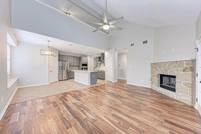 unfurnished living room featuring sink, a stone fireplace, high vaulted ceiling, ceiling fan with notable chandelier, and light wood-type flooring