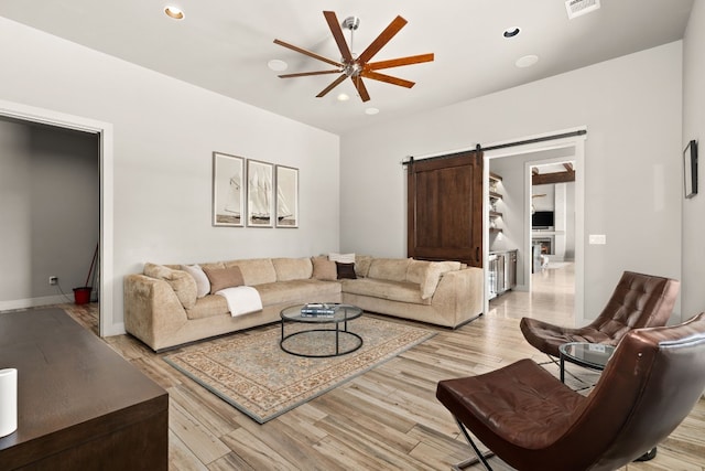 living room with a barn door, ceiling fan, and light hardwood / wood-style flooring