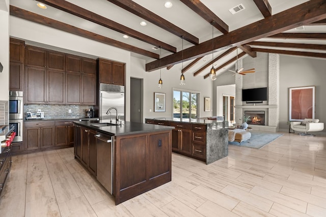 kitchen with a large fireplace, sink, an island with sink, and high vaulted ceiling