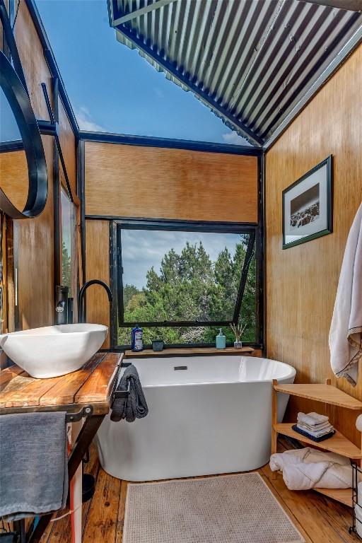 bathroom with a tub to relax in, wood walls, and wood-type flooring