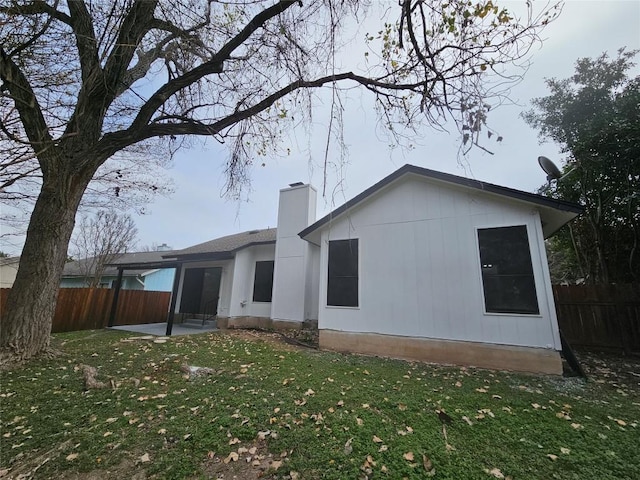 rear view of house with a patio area, fence, a chimney, and a lawn