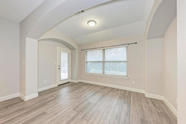 empty room with plenty of natural light, vaulted ceiling, and light hardwood / wood-style flooring