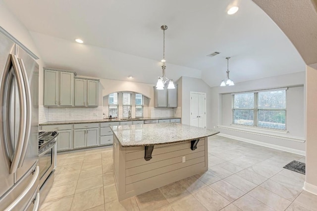 kitchen with light stone countertops, stainless steel appliances, sink, an inviting chandelier, and a kitchen island