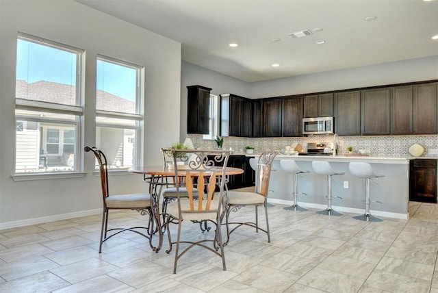 kitchen with backsplash, a breakfast bar, dark brown cabinets, and appliances with stainless steel finishes