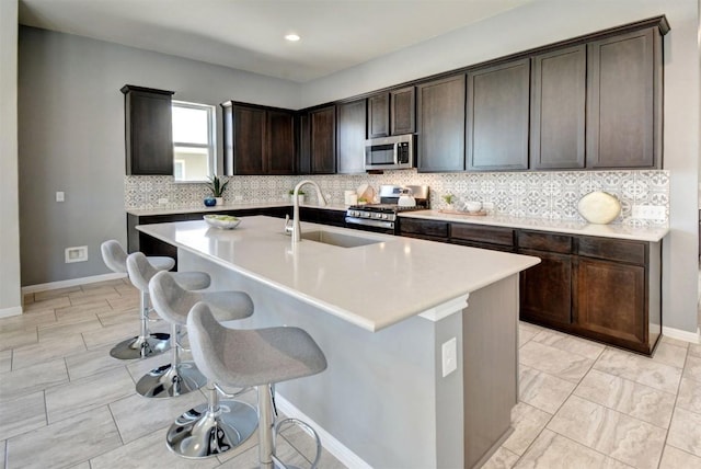 kitchen with dark brown cabinetry, a kitchen island with sink, sink, and stainless steel appliances