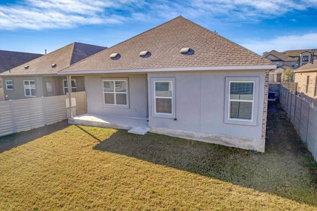 back of house with a shingled roof, a fenced backyard, a lawn, and stucco siding