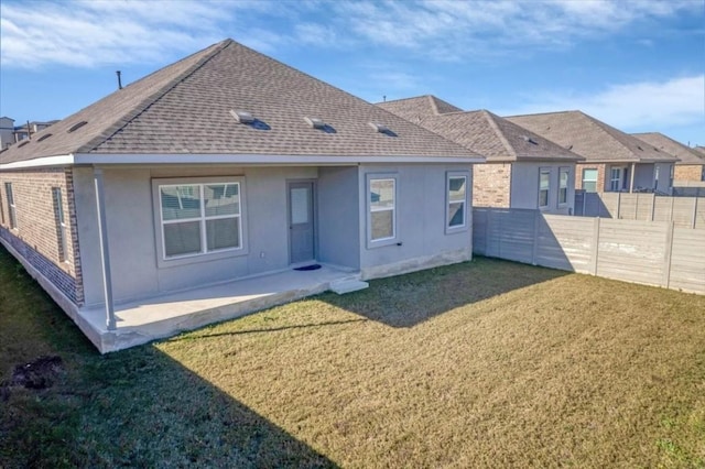 rear view of house with stucco siding, a fenced backyard, roof with shingles, a yard, and brick siding