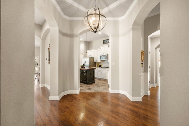 hallway featuring wood-type flooring, ornamental molding, and an inviting chandelier