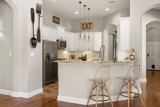 kitchen with kitchen peninsula, decorative light fixtures, a kitchen bar, white cabinets, and appliances with stainless steel finishes