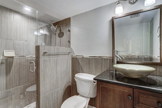 bathroom featuring vanity, toilet, a shower with shower door, and tile walls