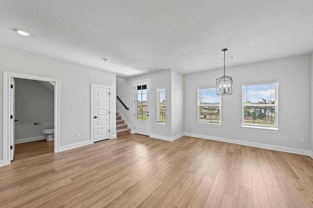 empty room with a healthy amount of sunlight, a chandelier, and light wood-type flooring