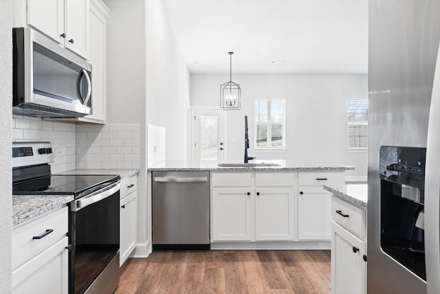 kitchen featuring pendant lighting, appliances with stainless steel finishes, light stone counters, white cabinets, and dark hardwood / wood-style flooring