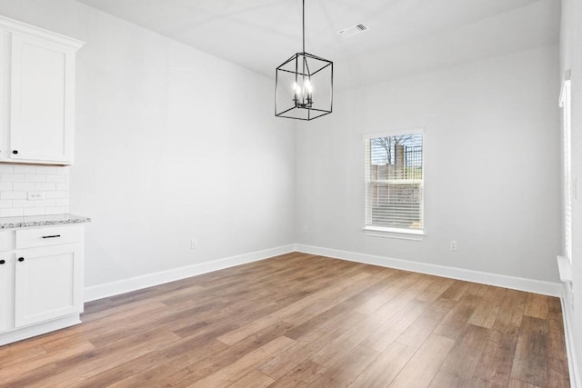 unfurnished dining area with a notable chandelier and light hardwood / wood-style flooring