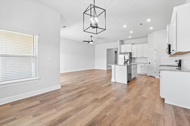 kitchen featuring ceiling fan with notable chandelier, decorative light fixtures, tasteful backsplash, an island with sink, and white cabinets