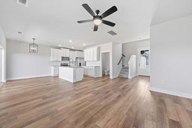 unfurnished living room featuring ceiling fan with notable chandelier, sink, and light hardwood / wood-style flooring