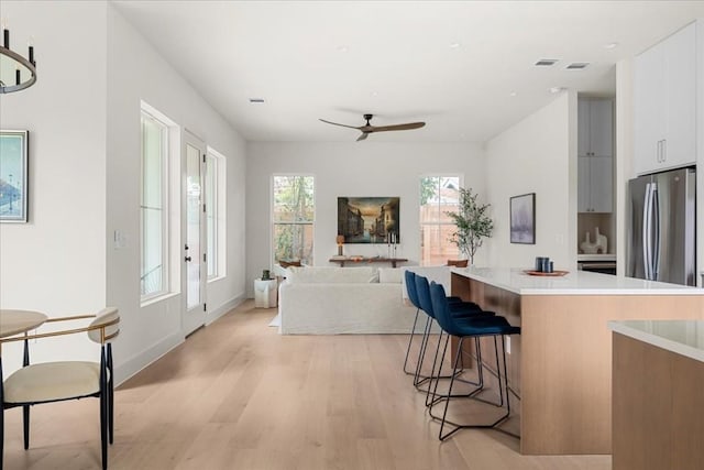 kitchen featuring ceiling fan, stainless steel fridge, a breakfast bar, white cabinets, and light wood-type flooring