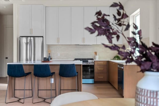 kitchen with white cabinetry, sink, stainless steel appliances, light hardwood / wood-style floors, and decorative backsplash