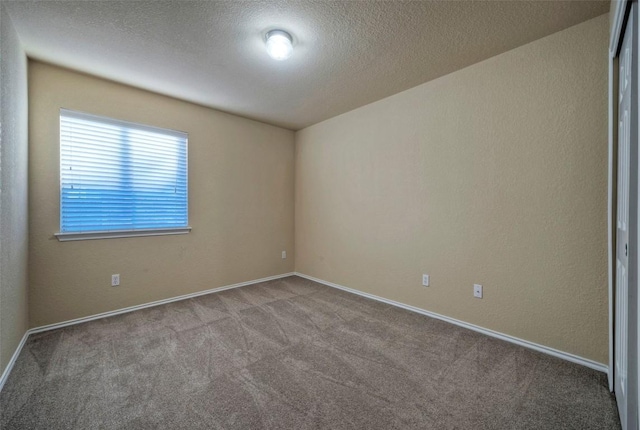 carpeted empty room with a textured ceiling, a textured wall, and baseboards