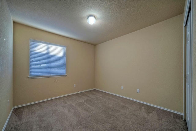 carpeted empty room featuring a textured ceiling, a textured wall, and baseboards