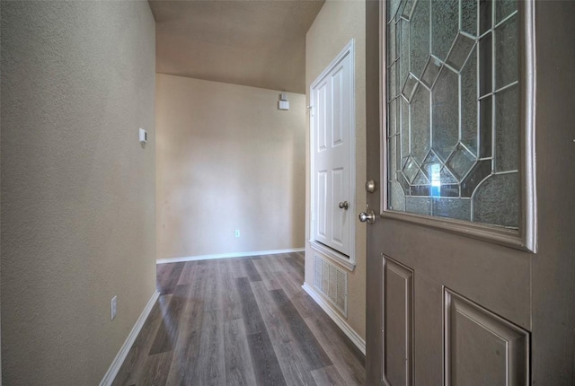 doorway featuring dark wood-type flooring, a textured wall, and baseboards