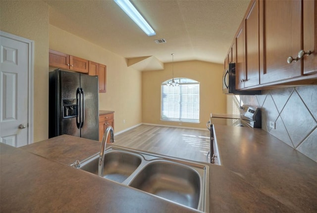 kitchen featuring a sink, visible vents, stainless steel range with electric cooktop, black fridge, and brown cabinetry