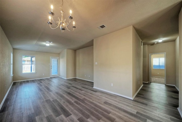 spare room with dark wood-type flooring, a chandelier, visible vents, and baseboards