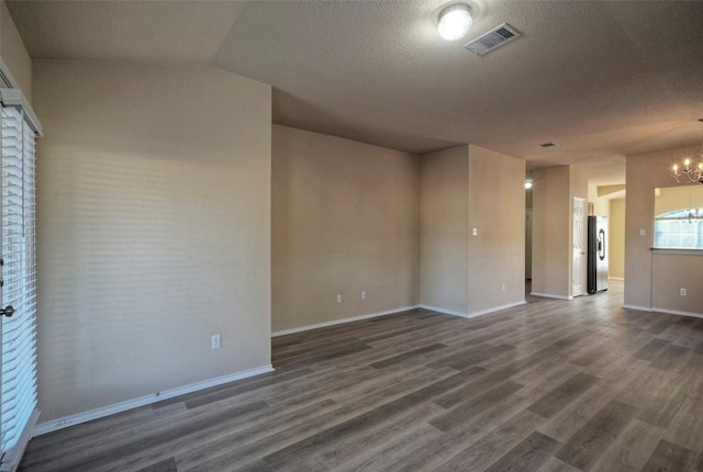 spare room featuring dark wood-style floors, visible vents, a chandelier, and a textured ceiling