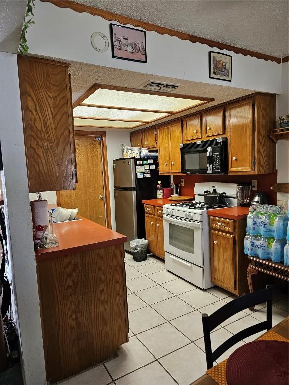 kitchen featuring light tile patterned floors, a textured ceiling, stainless steel refrigerator, and white gas range