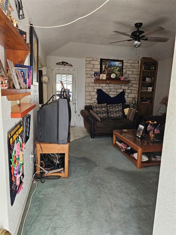 living room with carpet floors, a stone fireplace, ceiling fan, and lofted ceiling