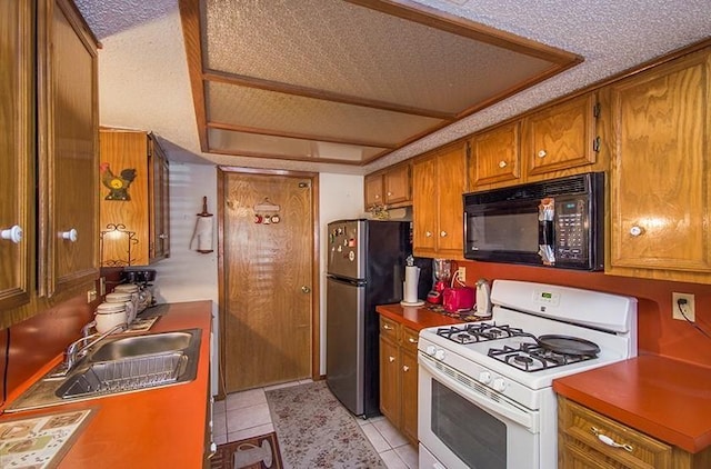 kitchen with stainless steel refrigerator, white gas range, sink, a textured ceiling, and light tile patterned floors