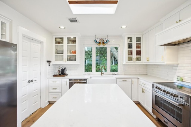 kitchen featuring a skylight, white cabinetry, stainless steel appliances, and decorative backsplash