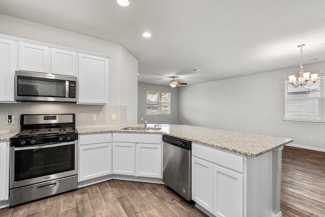 kitchen featuring stainless steel appliances, a peninsula, dark wood-style flooring, a sink, and white cabinets